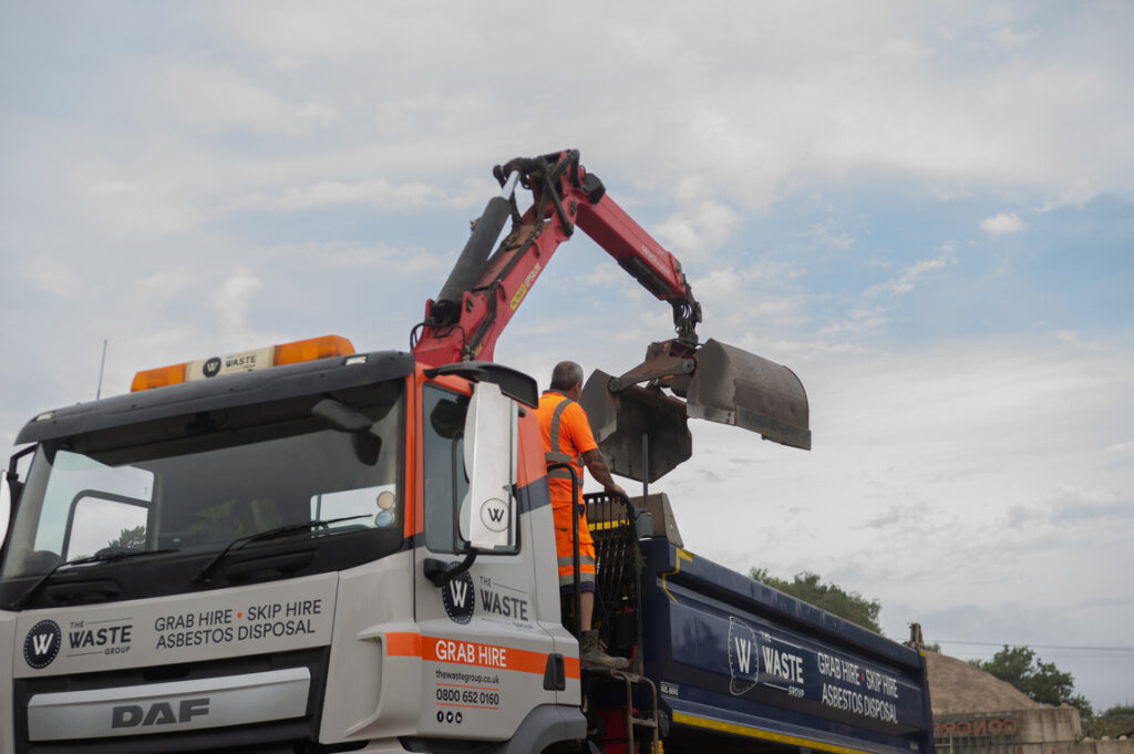 a grab lorry with a worker, the waste group logo and contact info on the lorry